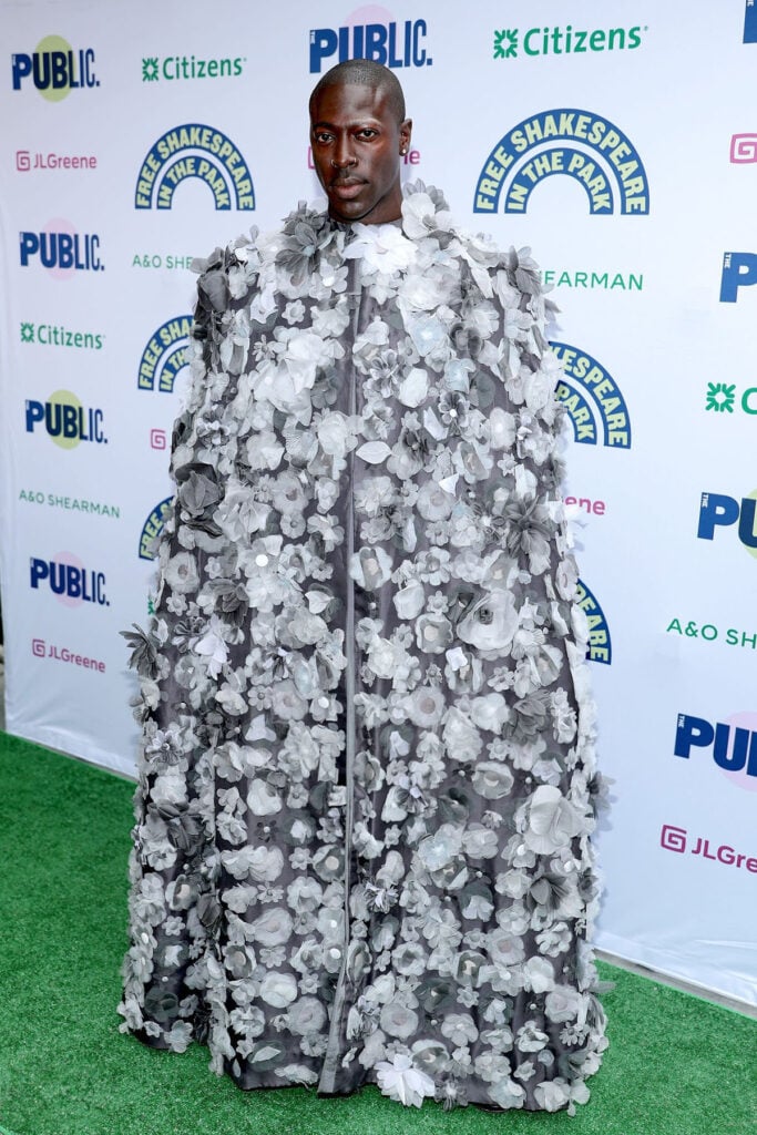 Moses Sumney attends Shakespeare in the Park's opening night celebration of "Twelfth Night"  Thom Browne Spring 2022 floral cape. Lupita Nyong’o Chanel, Moses Sumney Thom Browne, Sandra Oh CFCL, Shakespeare in the Park red carpet, Twelfth Night premiere, celebrity style 
