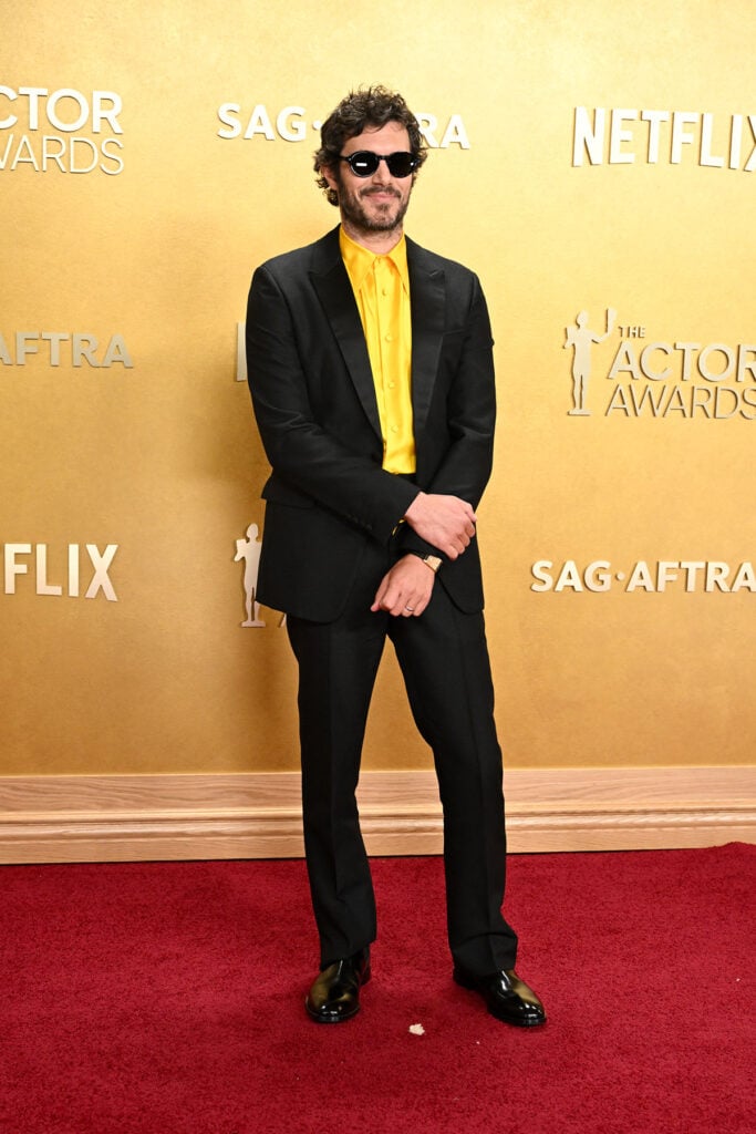 Adam Brody Prada Actor Awards 2026, black Prada suit yellow silk shirt, Adam Brody red carpet style, Cartier Tank à Guichets, statement menswear, bold shirt styling, contemporary tailoring