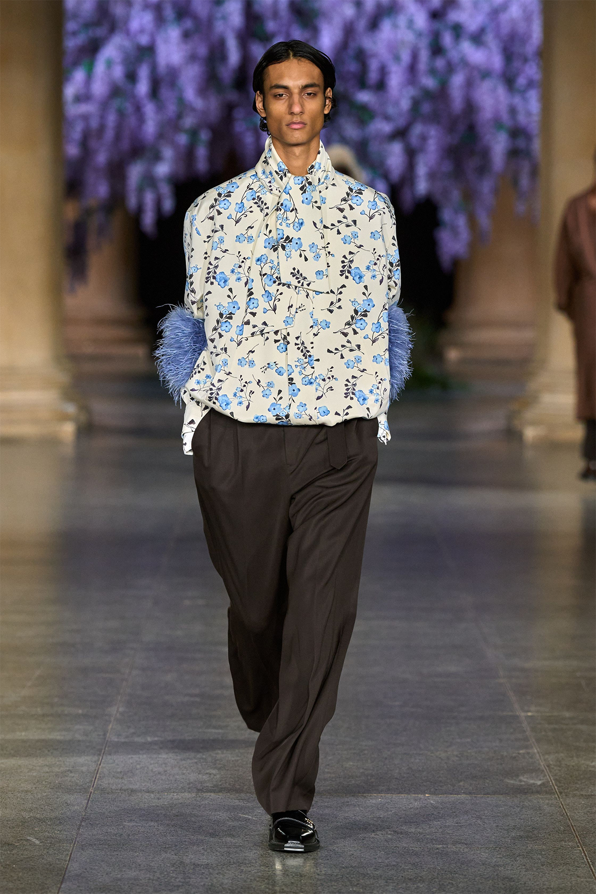 Mithridate Fall 2026 runway look featuring a floral-print Lavallière shirt, blue feathered cuffs and black wide-leg trousers.