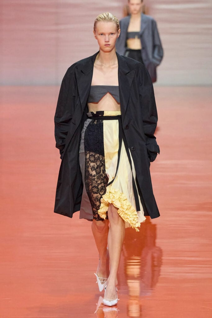 Prada Spring 2026 runway look featuring a bandeau top, lace panel skirt and oversized coat reference image.