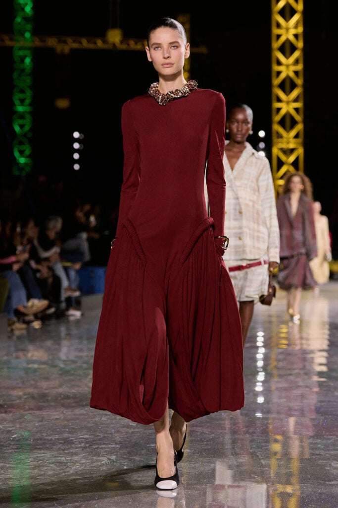 Chanel Fall 2026 garnet-red jersey crêpe dress with sculptural pleated skirt panels on the runway.