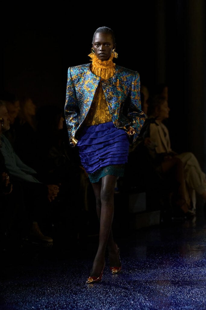 Saint Laurent Spring 2025 runway look featuring a brocade jacket, lace blouse, and tiered cobalt skirt.