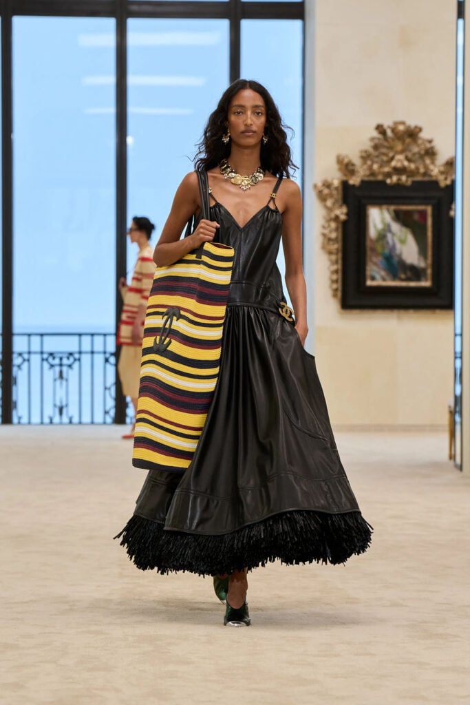 Chanel Resort 2027 black leather dress with raffia-trimmed skirt shown on the runway.