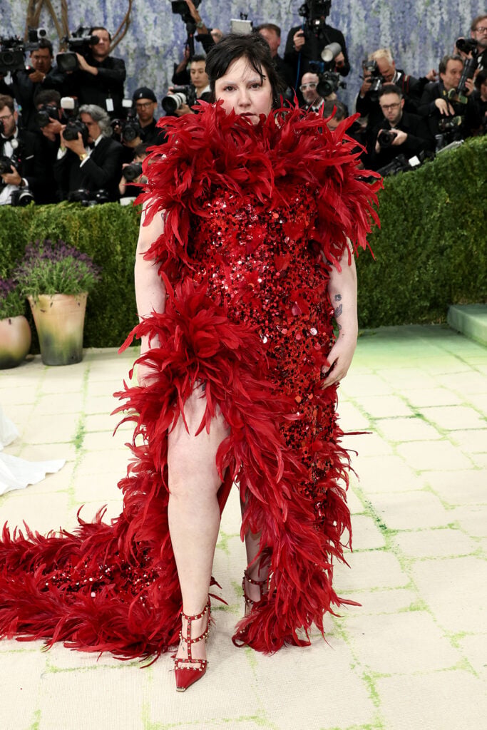 Lena Dunham wearing red sequinned Valentino gown with feather trim at the Met Gala