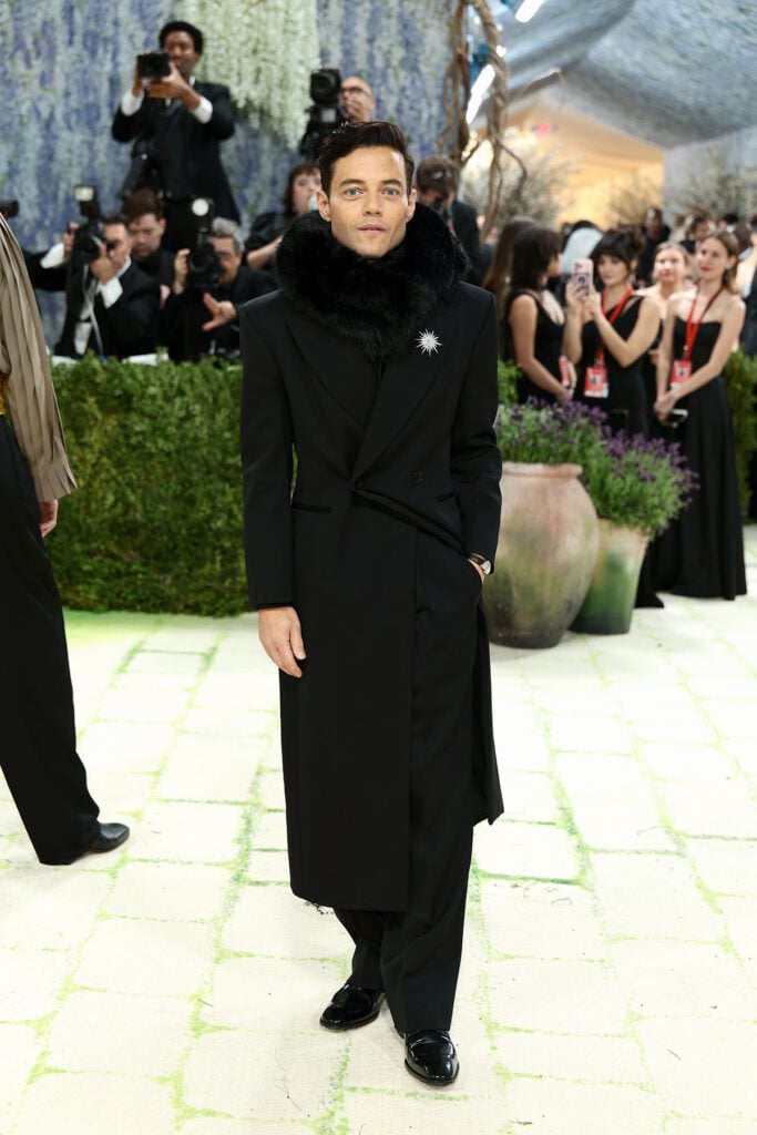 Rami Malek in black Saint Laurent coat with fur collar, Met Gala 2026