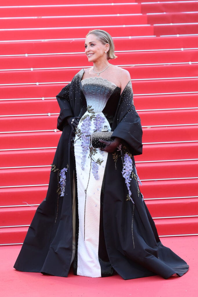 Sharon Stone posing in a black-and-white embroidered couture gown with dramatic cape on the Cannes red carpet.