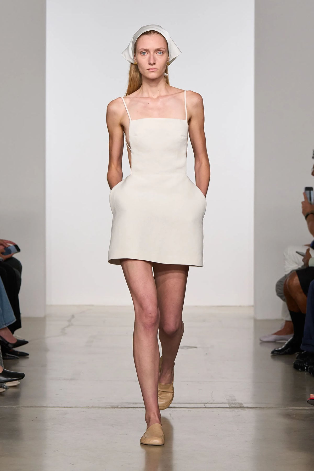 Calvin Klein Collection Spring 2026 runway look featuring the white apron-style mini dress and headscarf worn by Kate Mara.