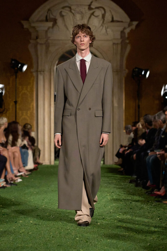Look de pasarela de Valentino con abrigo largo color topo, camisa a rayas y corbata burdeos.