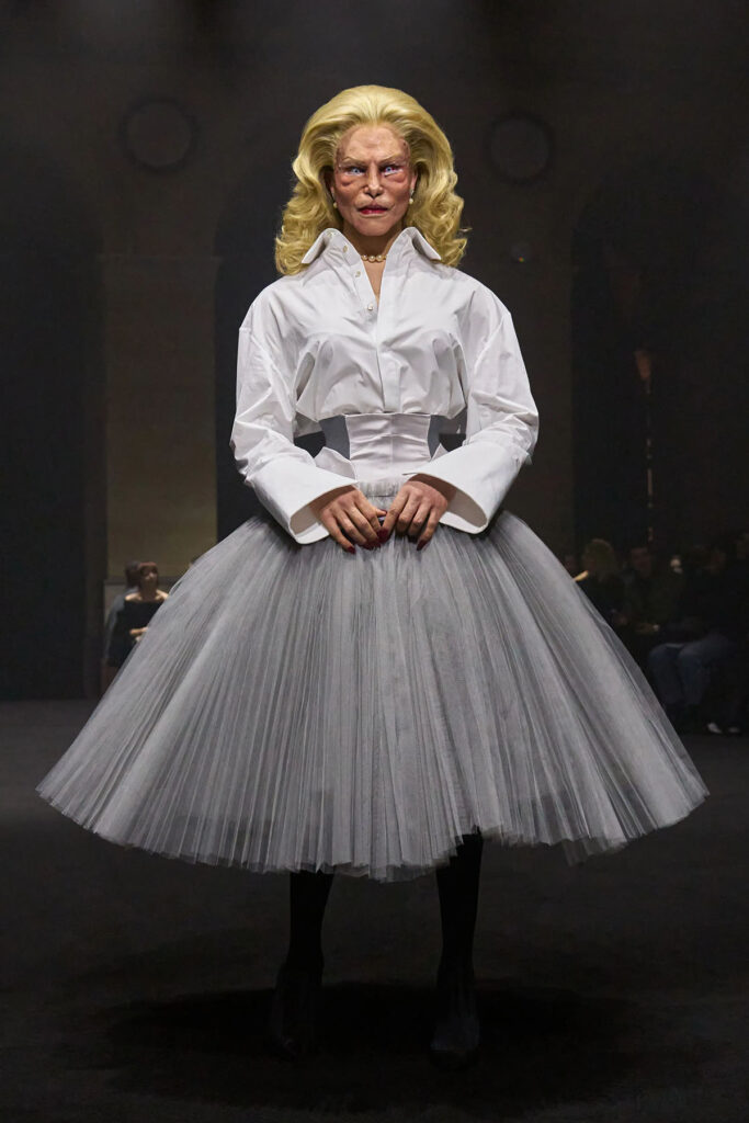Matières Fécales runway look featuring a white shirt, corseted waist and grey tulle skirt.