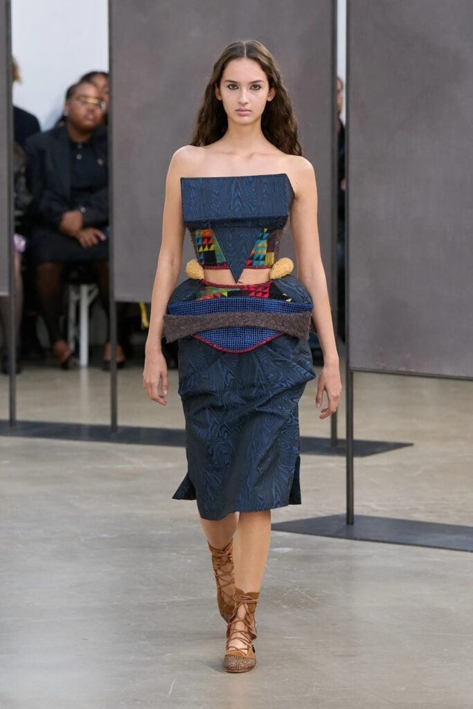 Kiko Kostadinov runway look featuring layered textiles and sculptural peplum detailing.