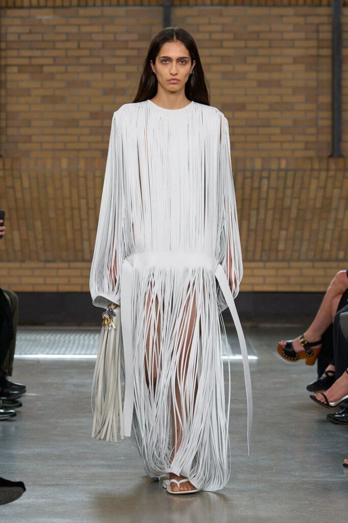 Model walks the Calvin Klein Collection Spring 2026 runway wearing the white laser-cut leather fringe dress