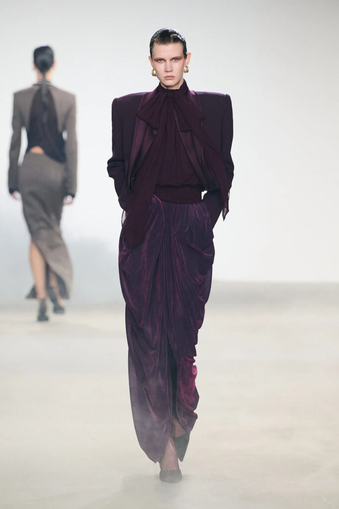 Model wears a plum draped look from the Oude Waag Fall 2026 collection on the runway.