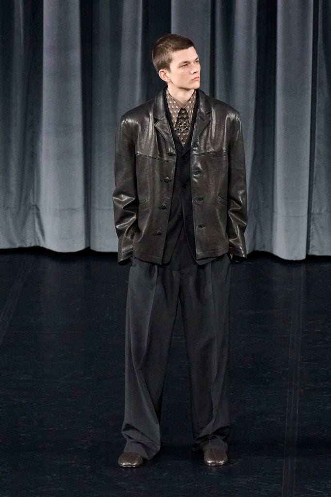 Lemaire Fall 2026 menswear look featuring a patterned shirt, knit vest and relaxed tailoring on the runway.