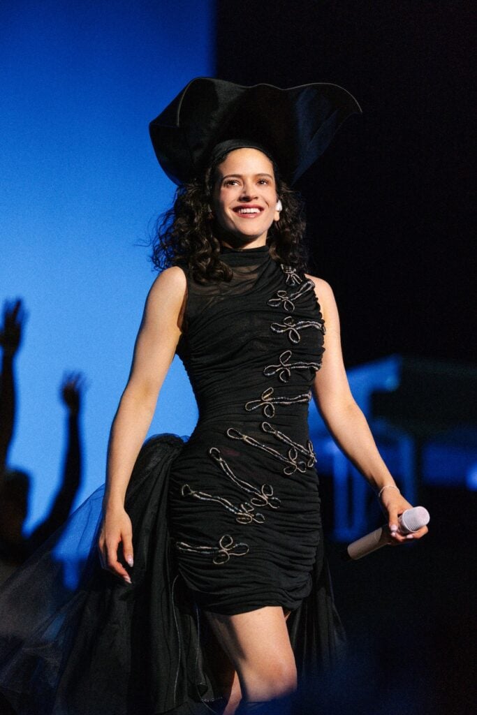 Rosalía performing on the LUX World Tour wearing a custom black ruched Dior dress with a dramatic tricorne-style hat