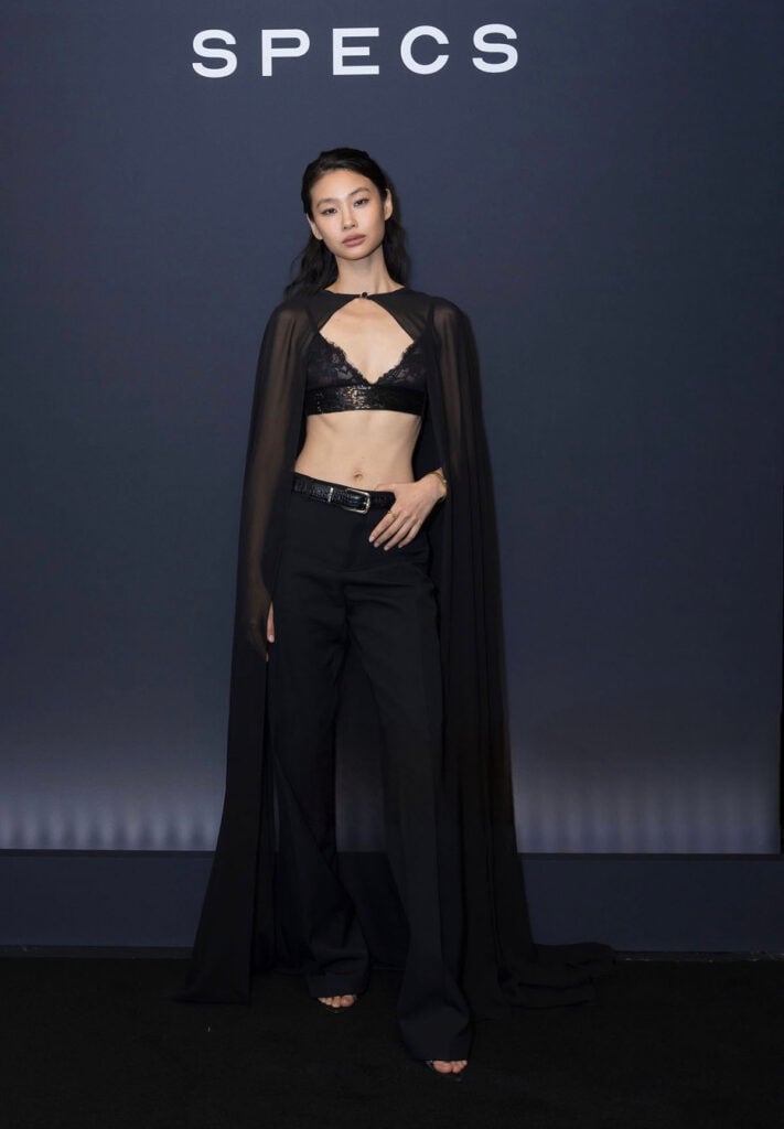 Hoyeon wearing Elie Saab Pre-Fall 2026 with a lace bralette, tailored trousers and sheer cape in Paris