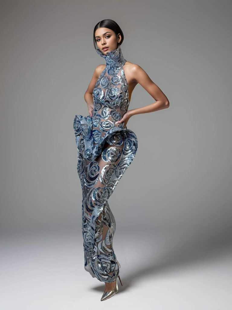 Model showcases a blue embellished Mitiliane Couture gown with a dramatic peplum detail.