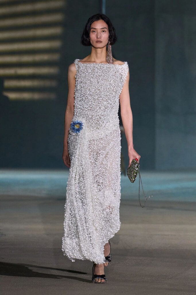 Mia Goth showcases her Dior Resort 2027 white draped dress with blue floral appliqué at The Odyssey London premiere.