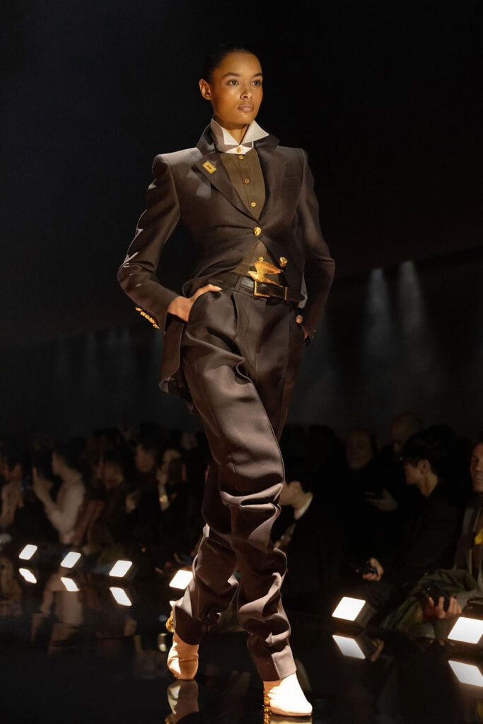 Model wearing the Schiaparelli Fall 2026 Haute Couture tailored look with elongated trousers on the runway.