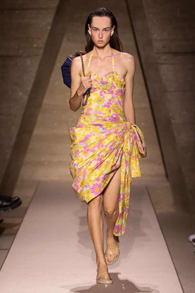Model walks the Chloé Spring 2026 runway wearing the floral draped halterneck dress with oversized side bow.