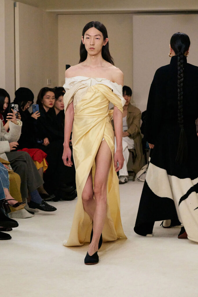 Samuel Gui Yang Fall 2026 off-the-shoulder gown on the runway featuring the draped neckline and wrap skirt.