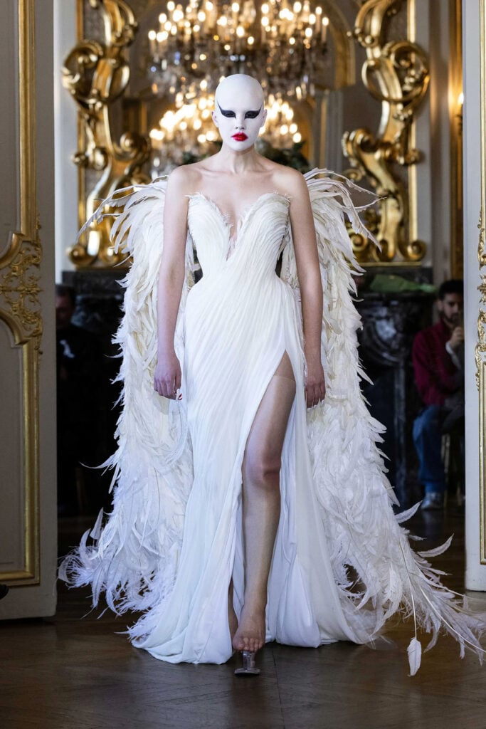 Matières Fécales Fall 2025 ivory feathered gown presented on the runway with sculptural winged detailing.
