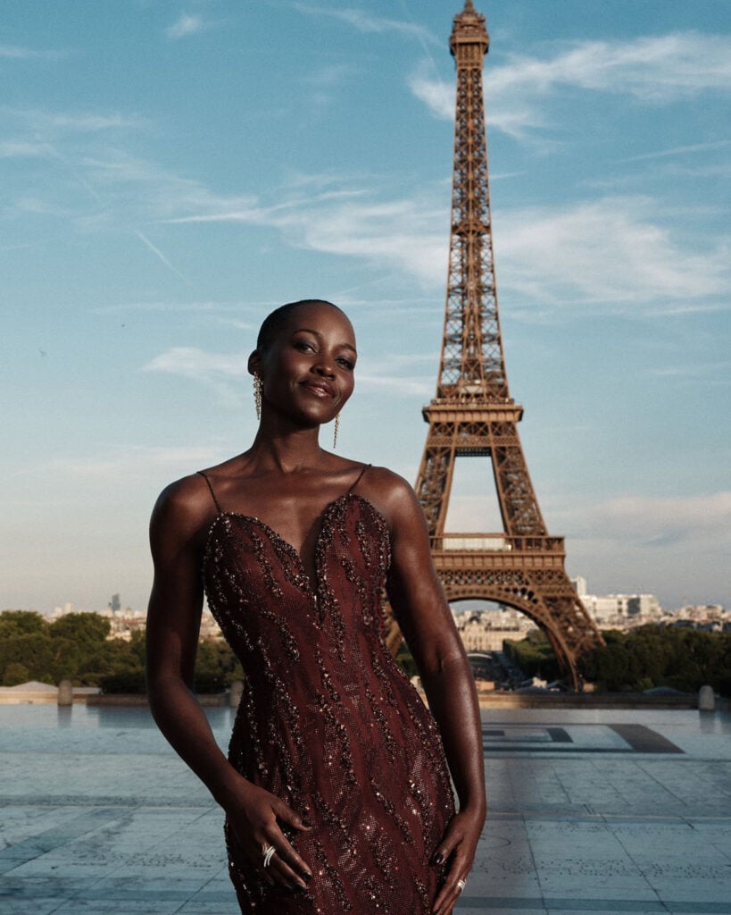 Lupita Nyong'o posing in a custom Armani Privé gown with the Eiffel Tower backdrop at The Odyssey Paris photoca