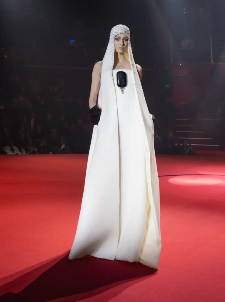 Model wearing the Stéphane Rolland Fall 2026 Couture white hooded column gown on the Paris runway.
