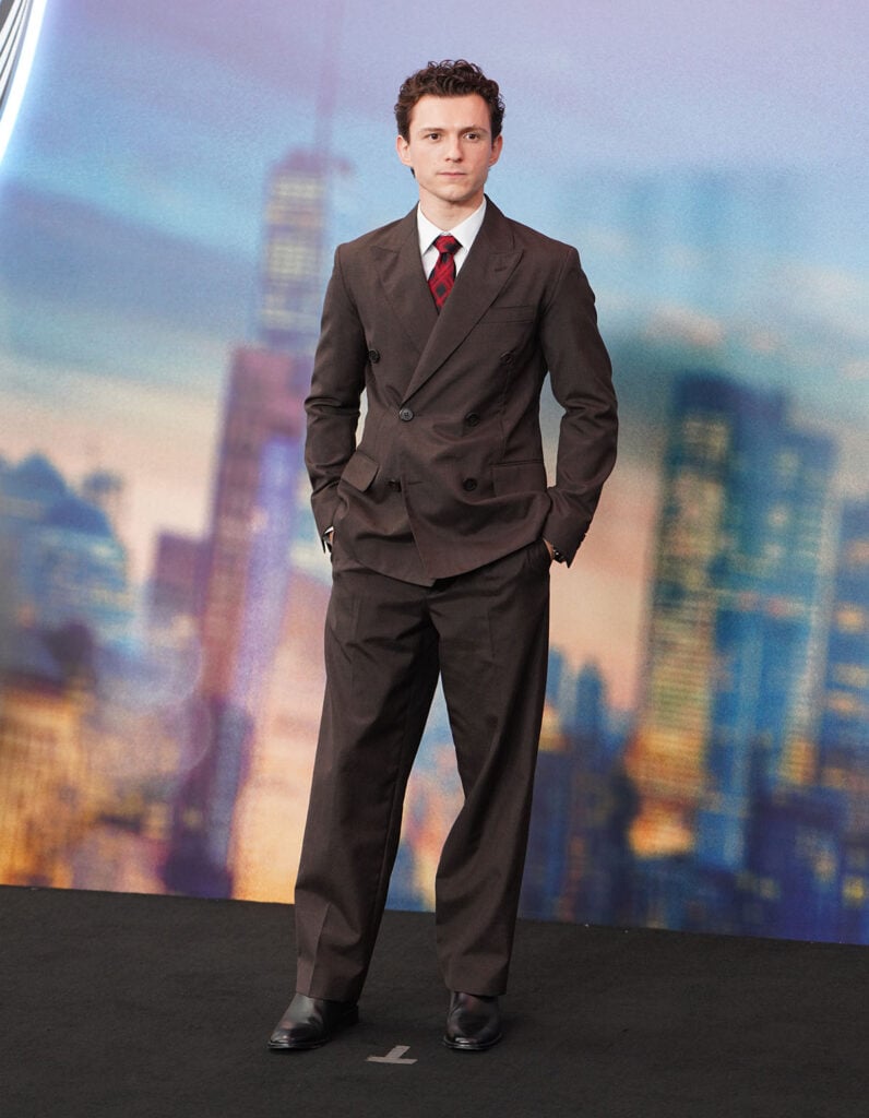 Tom Holland wearing a brown Prada suit and red striped tie at the Spider-Man: Brand New Day Shanghai photocall.