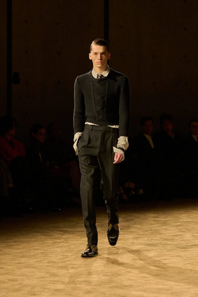 Saint Laurent Fall 2026 menswear look with a cropped cable-knit sweater, striped shirt and tailored trousers