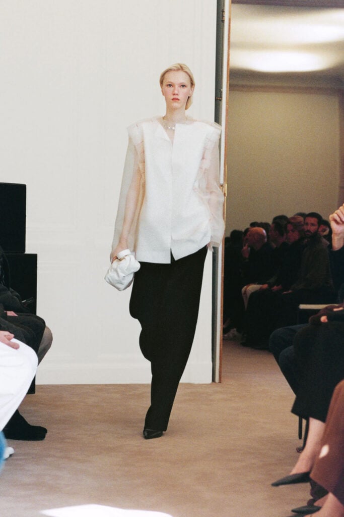 The Row Resort 2027 look featuring a white shirt with sheer tulle sleeves and visible red basting stitches.