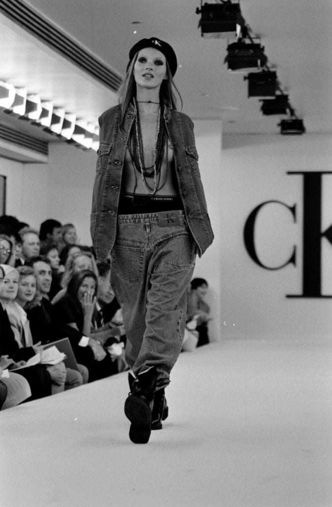 Kate Moss wearing backwards jeans and a denim waistcoat on the Calvin Klein Collection Spring-Summer 1993 runway.