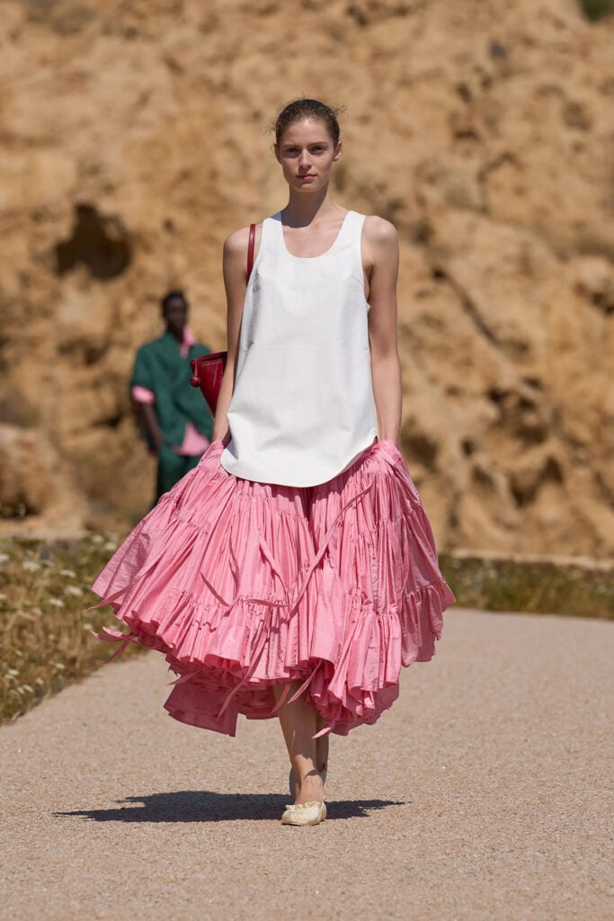 Jacquemus Spring 2027 runway look featuring a white tank top and pink tiered skirt with loose strips at the hem.