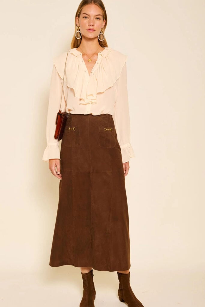 RIXO Edwina brown suede midi skirt with gold horsebit hardware, styled with an ivory ruffled blouse.