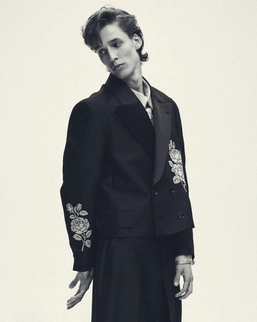 A model wears Viviano’s black cropped blazer featuring white cross-stitch floral embroidery.