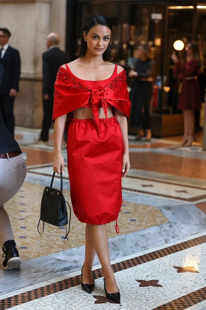 Camila Mendes wearing a custom red Prada look with a tie-front shawl, matching skirt and black accessories at Vogue World Milano.