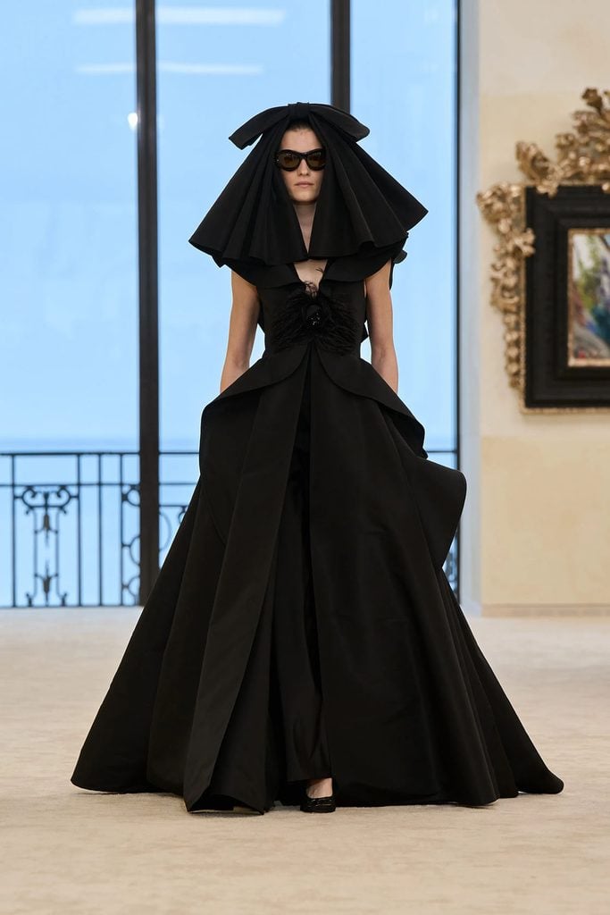 Chanel Resort 2027 runway look featuring the black gown with a feather-embellished camellia and voluminous skirt.