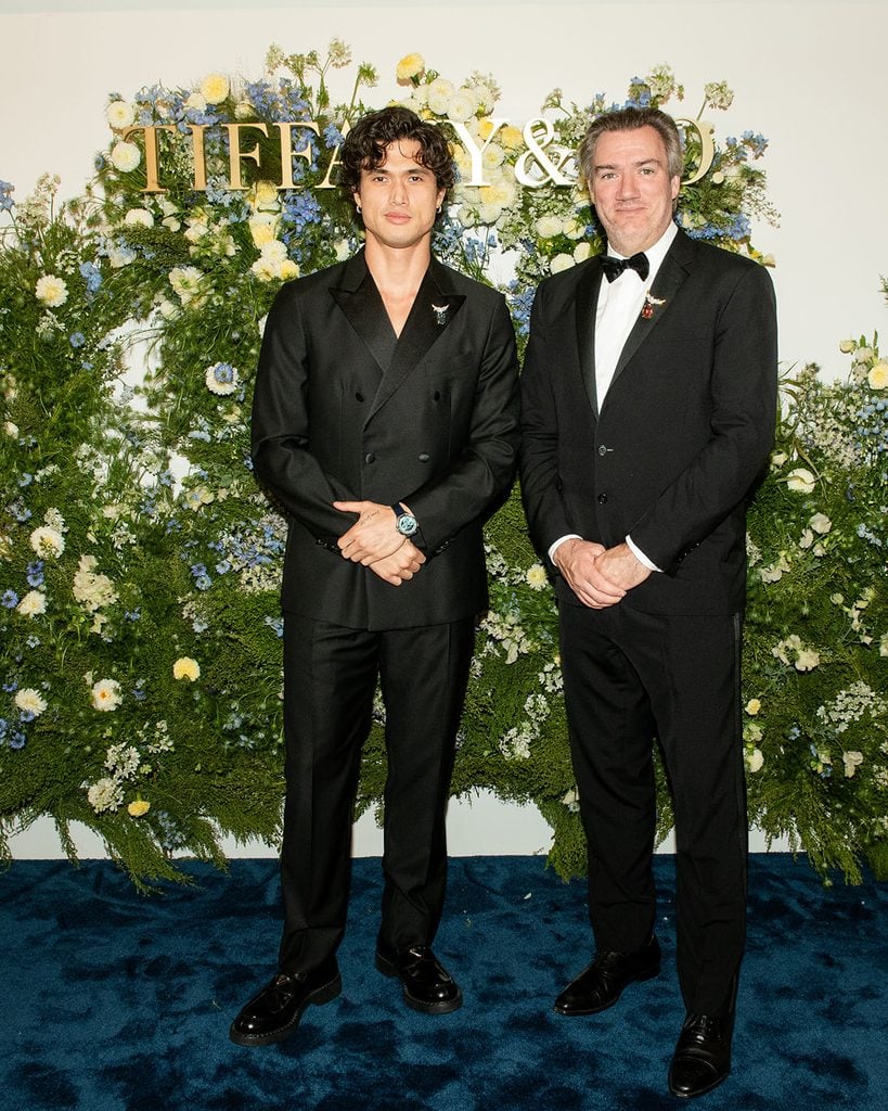 Charles Melton in a black Boglioli suit with a Tiffany & Co. brooch and watch beside a guest at the South Coast Plaza opening.