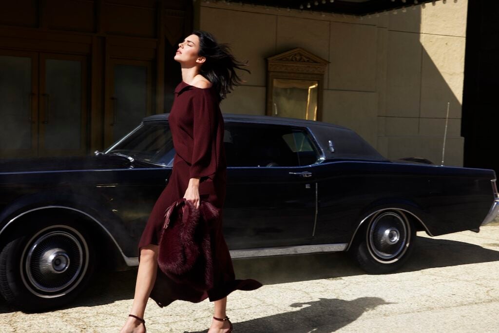 Kendall Jenner wears a black-cherry Donna Karan New York dress with sculptural gold jewellery for the Fall 2026 campaign.