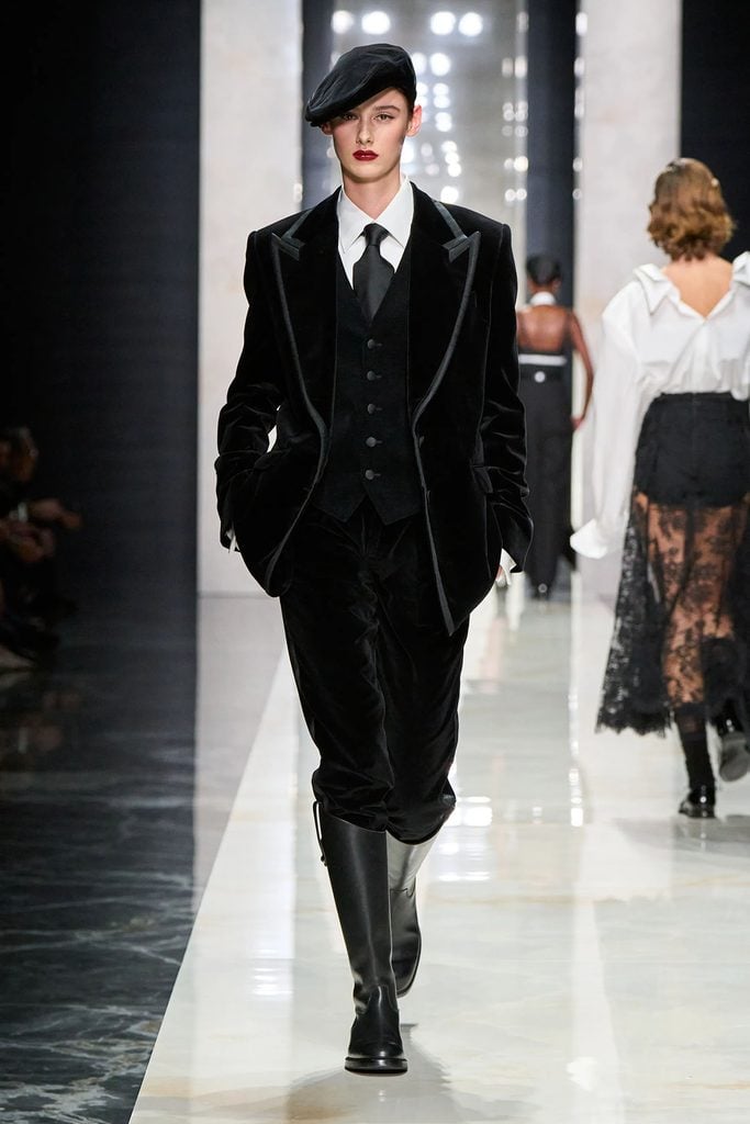 Dolce & Gabbana Fall 2026 runway look featuring a black velvet three-piece suit, tie, cap and knee-high boots.