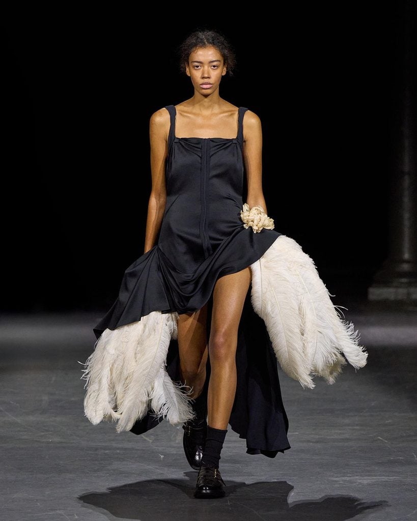 Erdem Resort 2027 black satin dress with oversized white feather plumes, floral hip detail, black socks and brogues on the runway