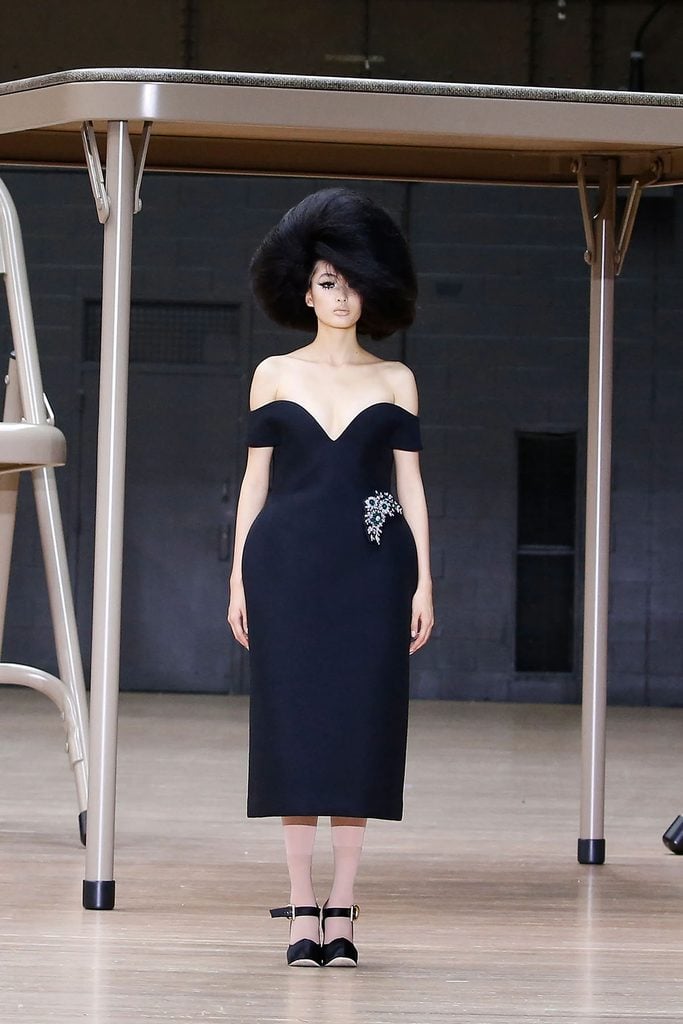 Marc Jacobs Spring 2024 runway look featuring an off-the-shoulder black dress with exaggerated hips and jewelled embellishment.