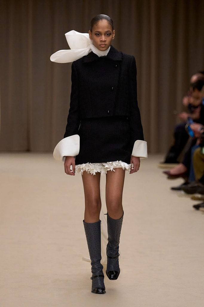 McQueen Fall 2026 runway look featuring black tailoring, an oversized ivory bow and floral-embroidered hem.