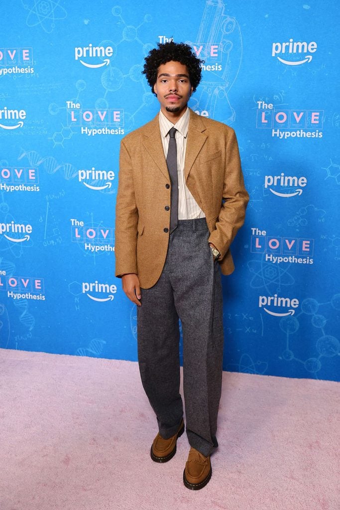 Nicholas Duvernay wearing a brown Dsquared2 blazer with grey trousers, a striped shirt, tie and Dr. Martens loafers at ‘The Love Hypothesis’ premiere.