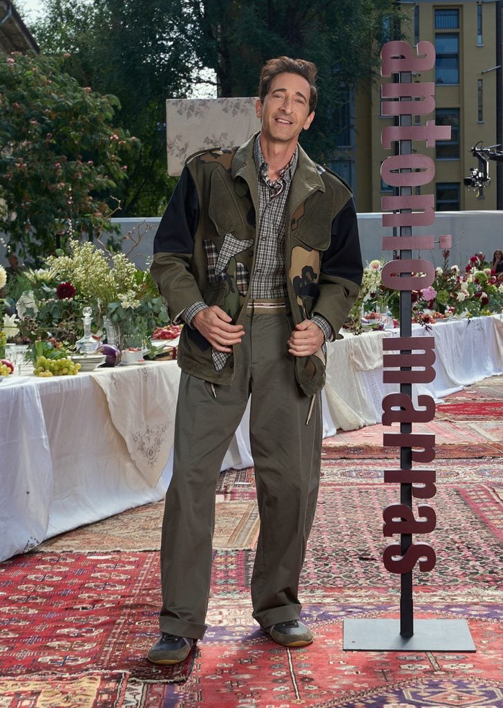 Adrien Brody wearing a layered Antonio Marras Spring 2027 look with a utility jacket and relaxed trousers at the designer’s Milan show