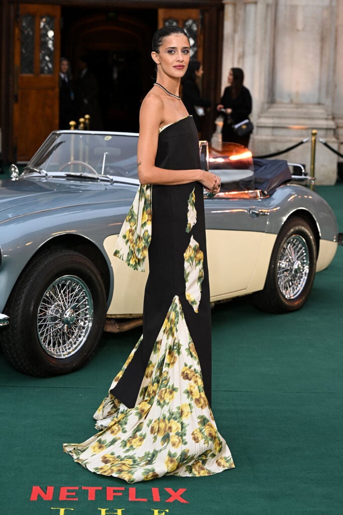Benedetta Porcaroli attends The Gentlemen Season Two world premiere in a black Prada column dress with floral-print taffeta details side view