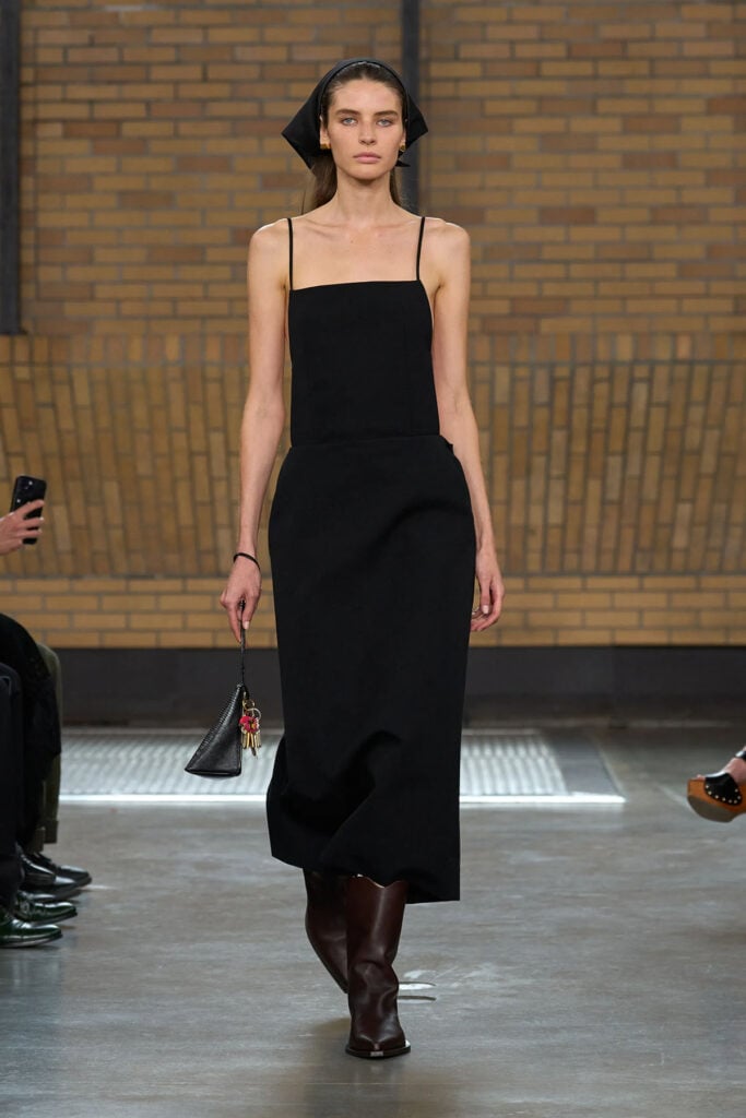 Calvin Klein Collection Spring 2026 runway look featuring the black apron-style dress and matching headscarf worn by Rooney Mara.