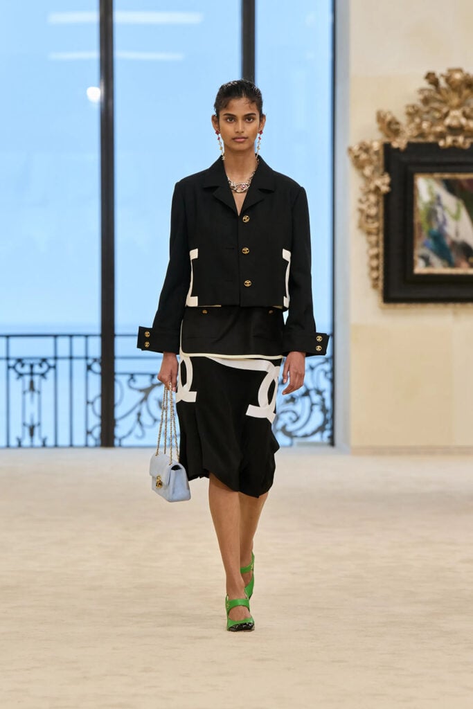 A model wears the black-and-white Chanel Resort 2027 jacket and skirt on the runway.