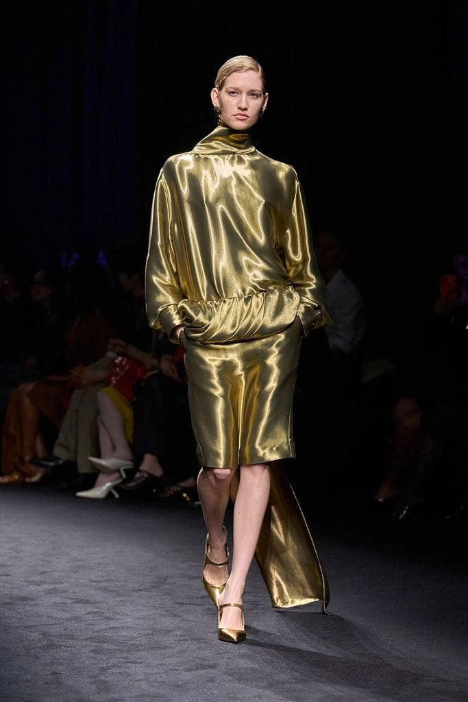 Ferragamo Fall 2026 runway look featuring a liquid-gold high-neck top and matching skirt with a draped waist detail.