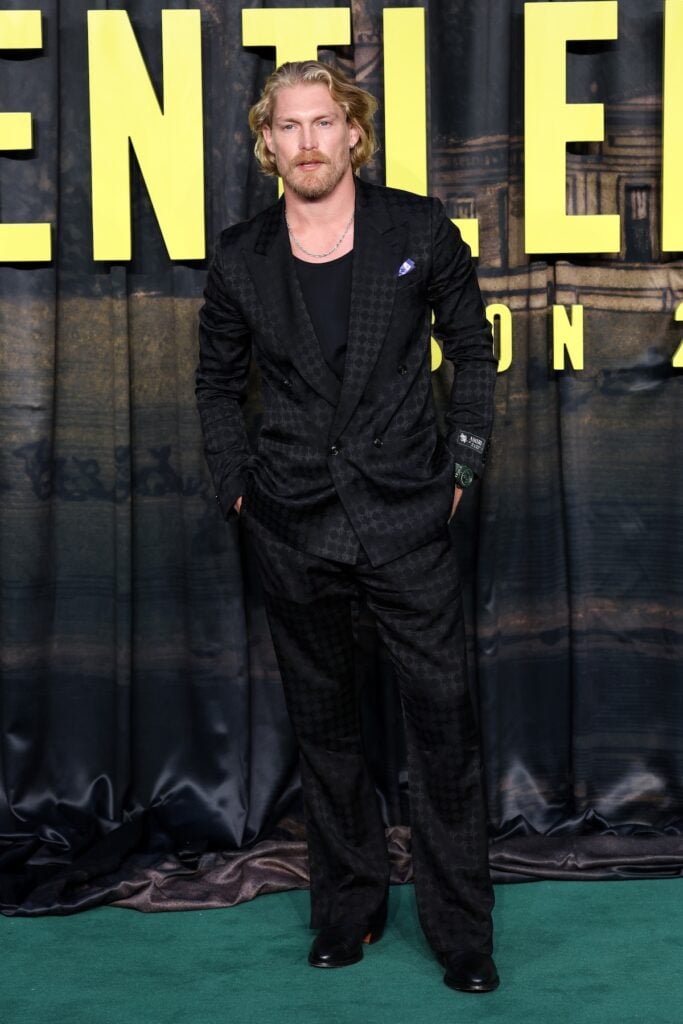 Harry Goodwins wears a black AMIRI monogram suit at The Gentlemen Season 2 premiere in London.
