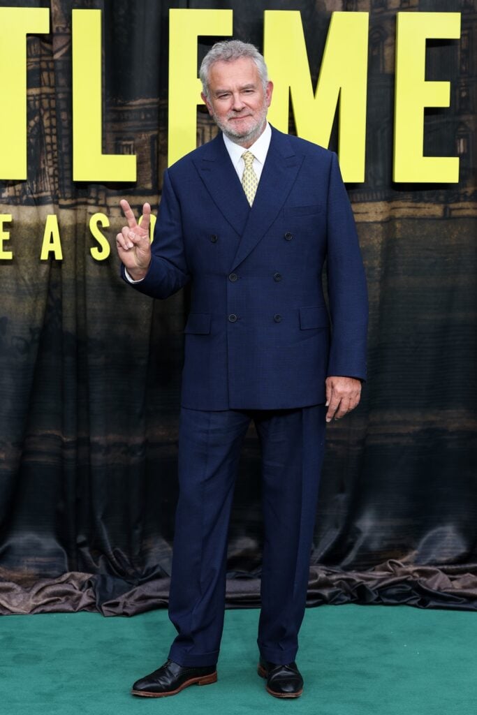 Hugh Bonneville wears a navy double-breasted suit with a yellow patterned tie at The Gentlemen Season 2 London premiere.